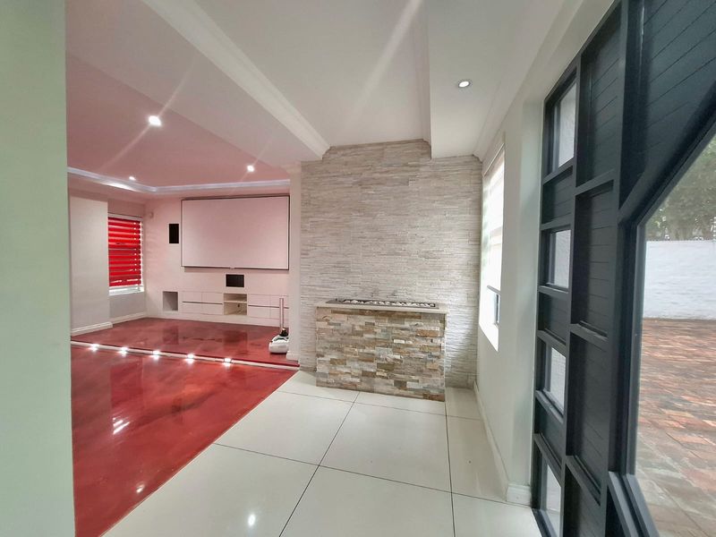 Spacious living area featuring a stone-clad fireplace, built-in media cabinetry, recessed lighting, and polished tiled flooring with direct access to the exterior.