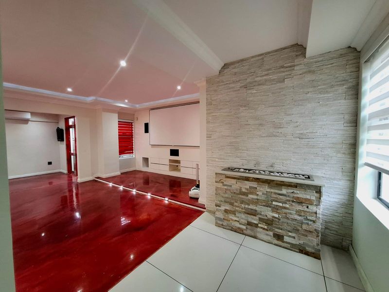 Spacious living area featuring a modern stone-clad fireplace, built-in media cabinetry, projector screen, and a combination of polished epoxy and tiled flooring.