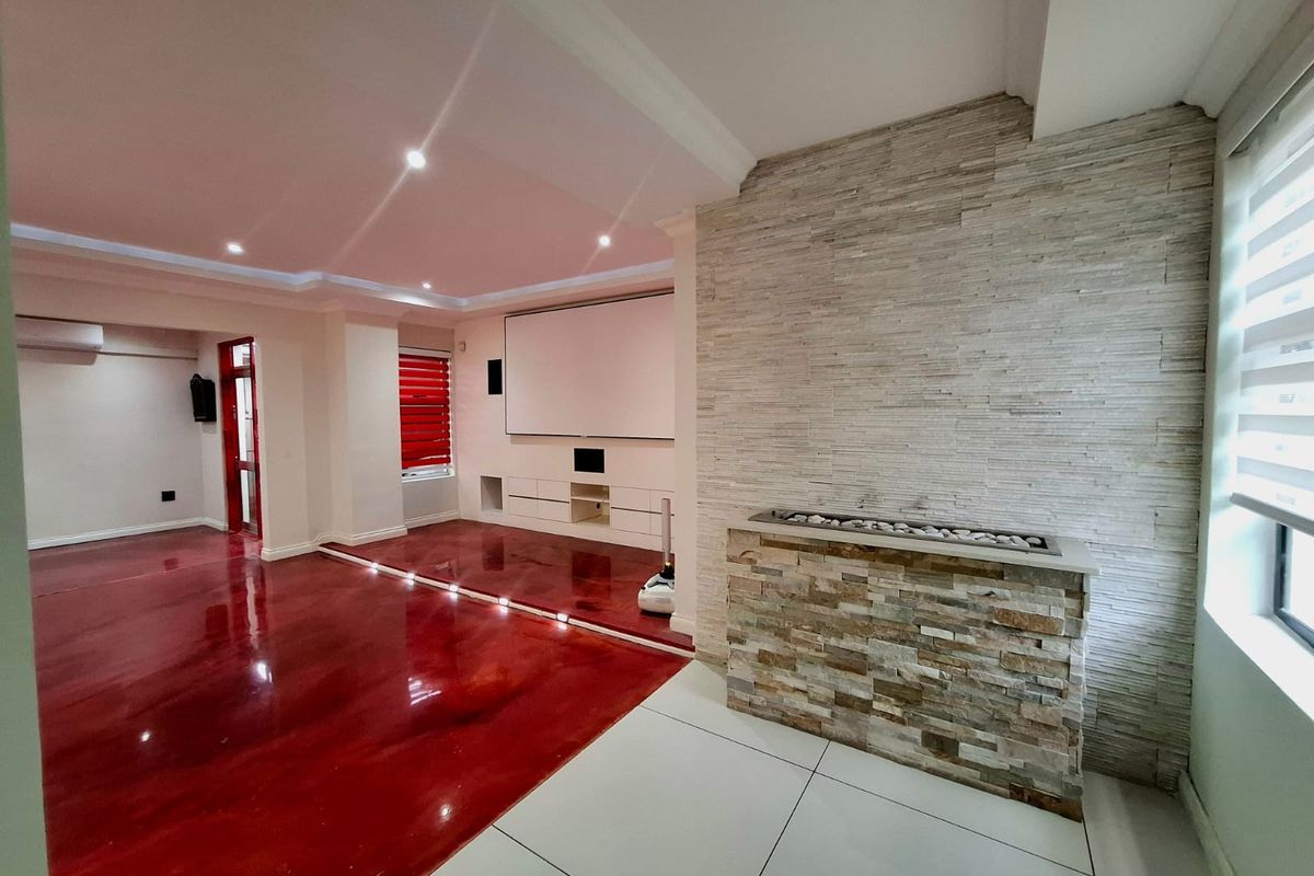Spacious living area featuring a modern stone-clad fireplace, built-in media cabinetry, projector screen, and a combination of polished epoxy and tiled flooring.