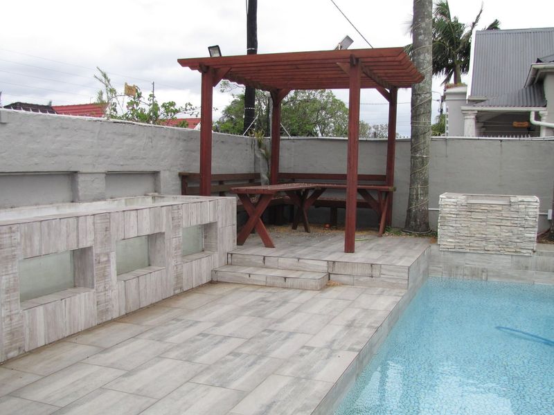 Outdoor pool area featuring a tiled deck, wooden pergola, and built-in stone cladding, enclosed by a perimeter wall with electric fencing.