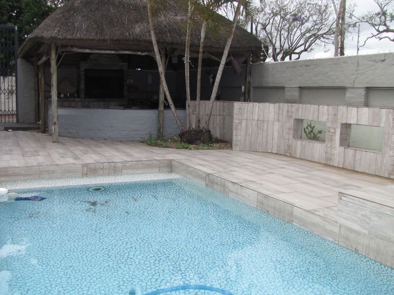Outdoor pool area featuring a tiled patio, a thatched lapa with a built-in braai, and a secure boundary wall.