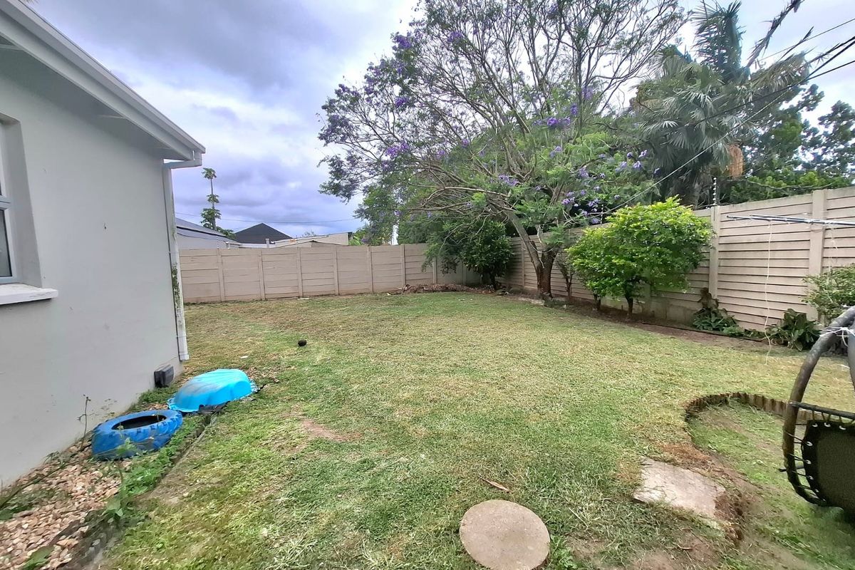 A rear garden area featuring a lawn, mature trees, and a precast concrete boundary wall.