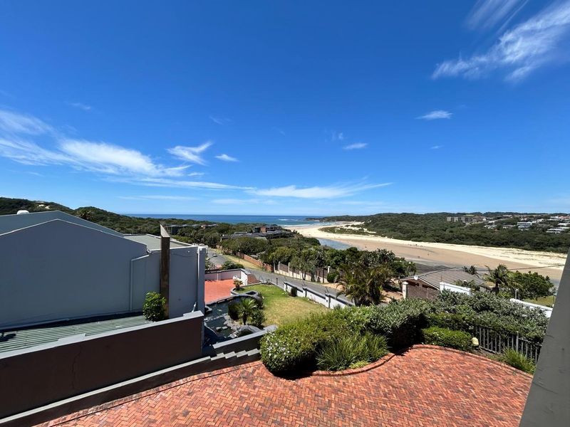 Elevated outdoor view overlooking the coastal landscape, beach, and surrounding residential area with a brick-paved patio in the foreground.