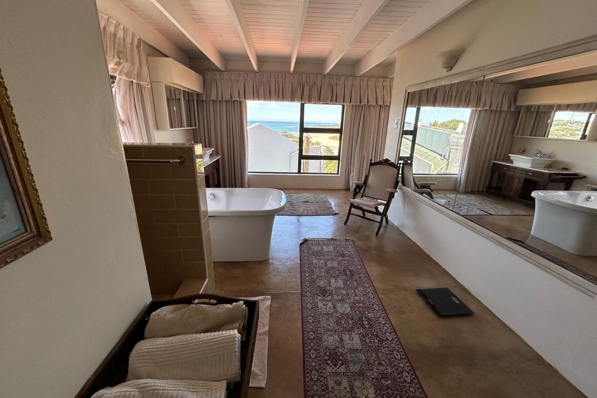 Spacious bathroom featuring a freestanding bathtub, vanity basin, and exposed beam ceiling, offering scenic coastal views through a large window.