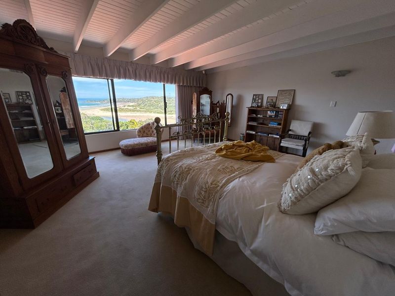 Spacious bedroom featuring exposed beam ceilings and a large sliding window offering expansive coastal and landscape views.