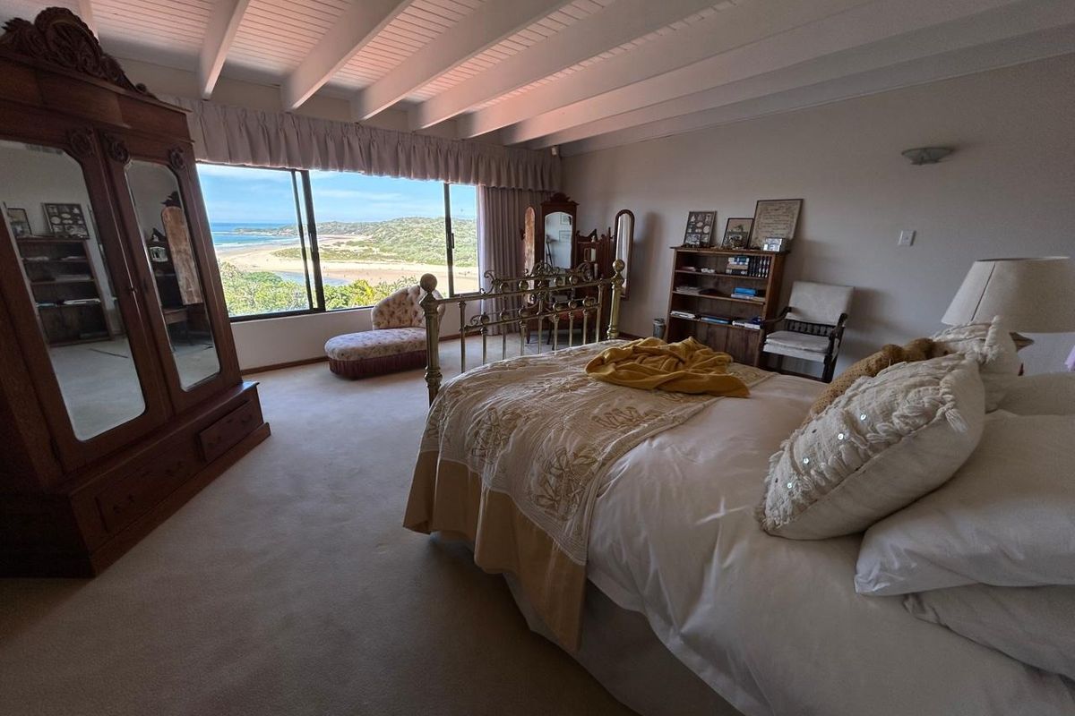 Spacious bedroom featuring exposed beam ceilings and a large sliding window offering expansive coastal and landscape views.