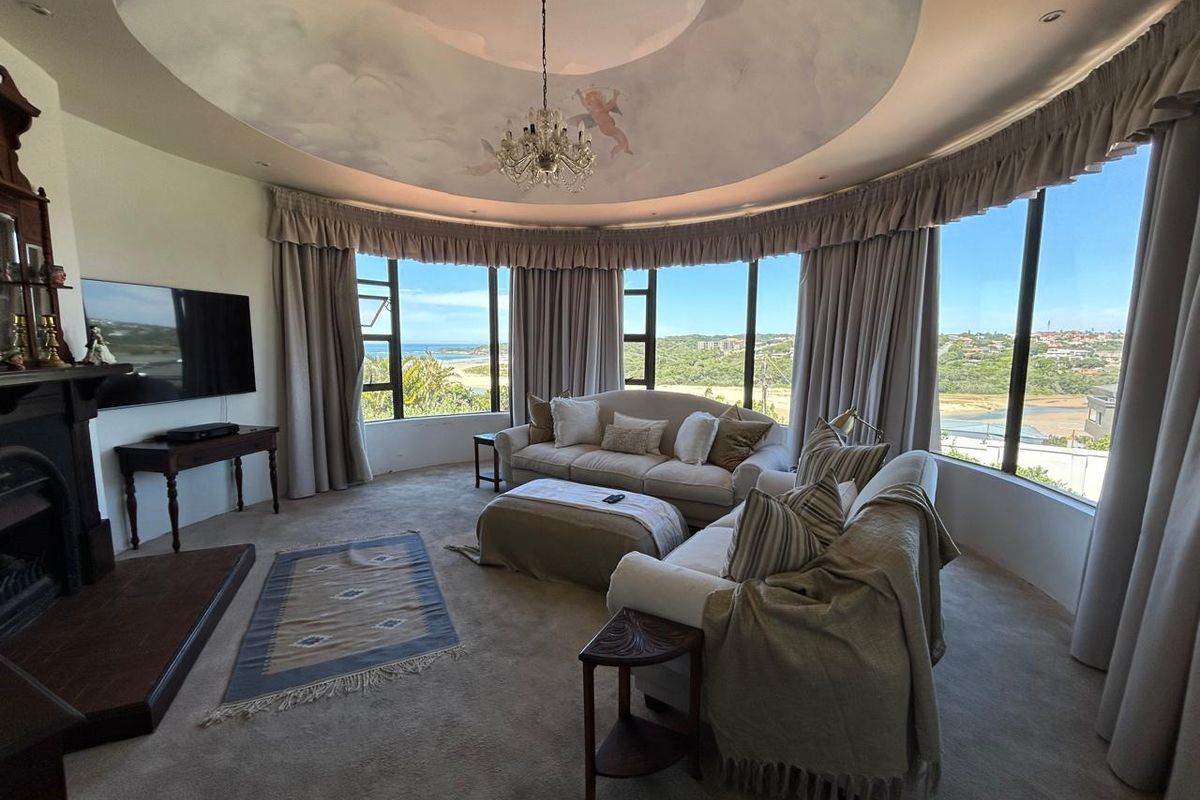 Spacious living room featuring a unique curved window wall with coastal views, a decorative ceiling dome, and a built-in fireplace.