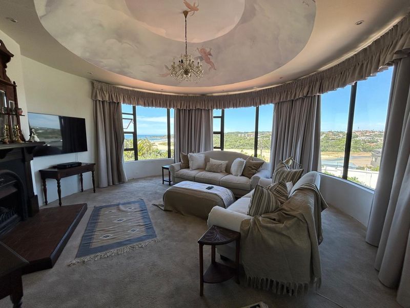Spacious living room featuring a unique curved window wall with coastal views, a decorative ceiling dome, and a built-in fireplace.