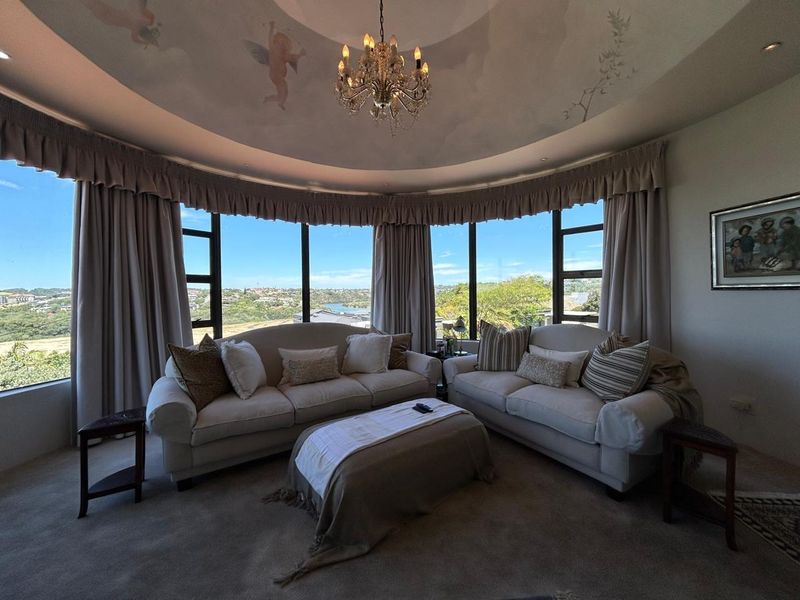A spacious living room featuring a unique curved wall with panoramic windows, a decorative painted ceiling mural, and recessed lighting.