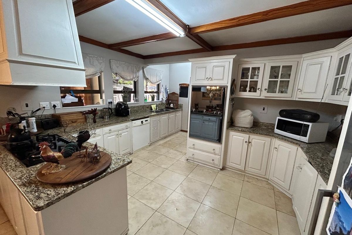 Spacious kitchen featuring granite countertops, built-in oven, ample cabinetry, and exposed timber ceiling beams, offering a functional layout with tiled flooring.