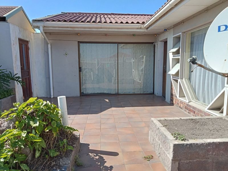 A paved outdoor patio area featuring a sliding glass door entrance, concrete planter boxes, and a tiled roof structure.