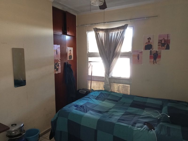 A bedroom featuring a built-in cupboard, tiled flooring, and a ceiling fan, requiring cosmetic updates to improve its overall appeal.