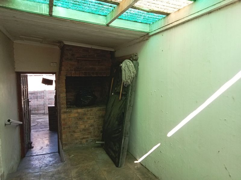 Covered patio area featuring a built-in brick braai, tiled flooring, and a translucent roof structure, offering a functional outdoor entertainment space.