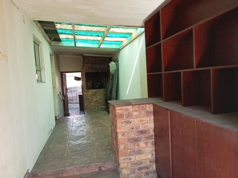 Covered patio area featuring a built-in brick braai, tiled flooring, and extensive built-in wooden shelving units.