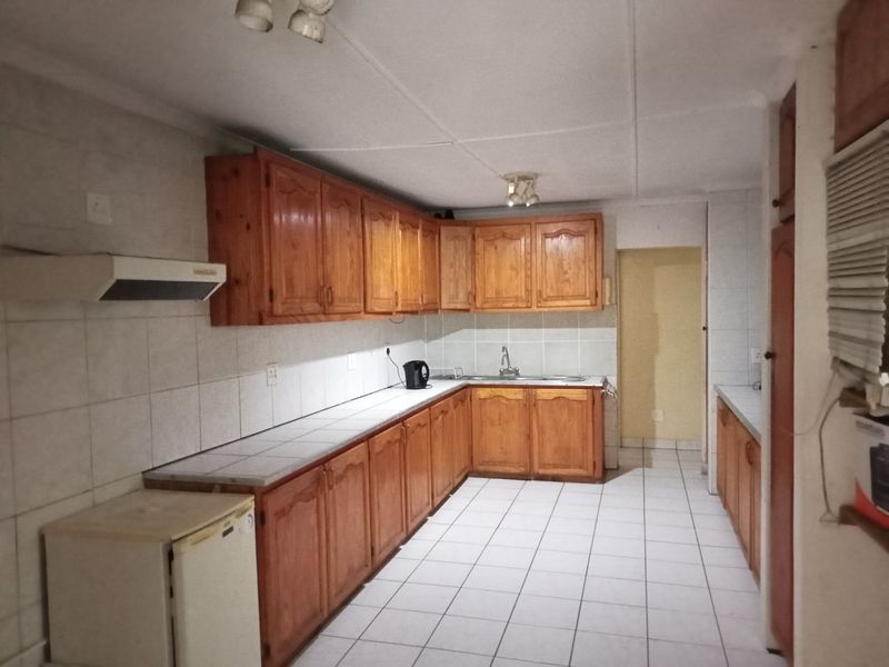 A functional kitchen featuring wooden cabinetry, tiled countertops, and tiled flooring, offering a classic layout with ample storage and workspace.