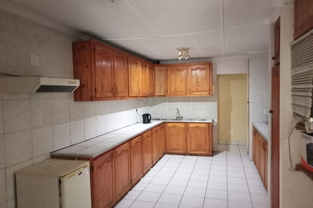 A functional kitchen featuring wooden cabinetry, tiled countertops, and tiled flooring, offering a classic layout with ample storage and workspace.