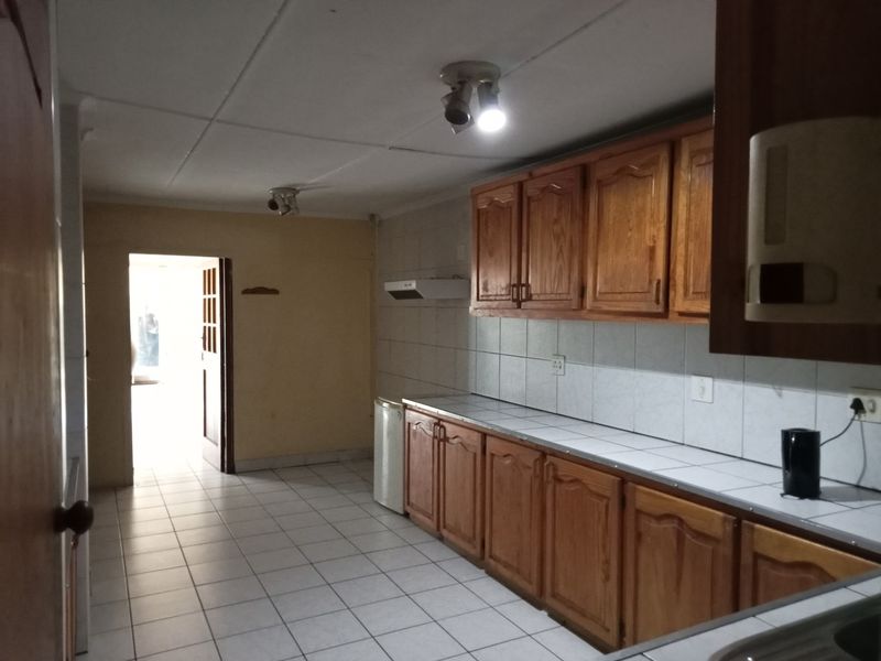 A functional kitchen featuring wooden cabinetry, tiled countertops, and tiled flooring, offering a clean and practical space ready for updates.