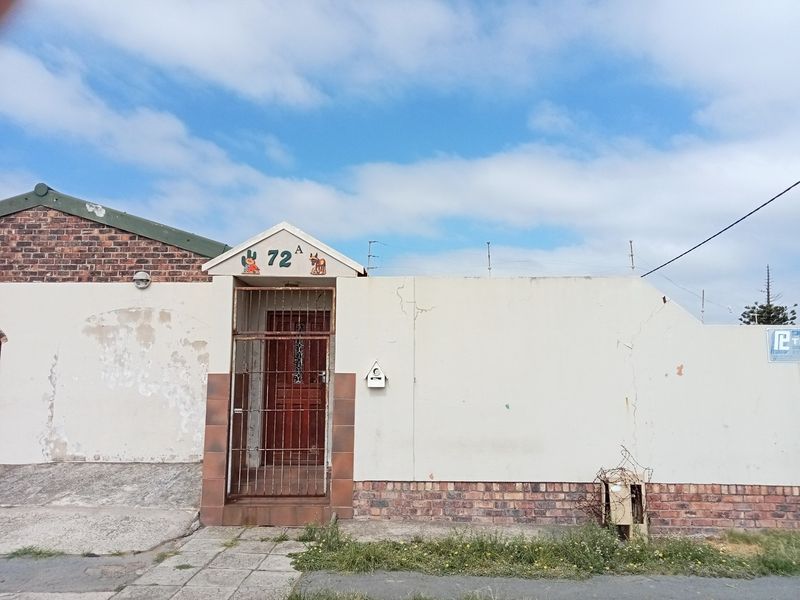 Front exterior view of the property featuring a secure entrance gate, brick boundary wall, and plastered facade with visible signs of weathering.