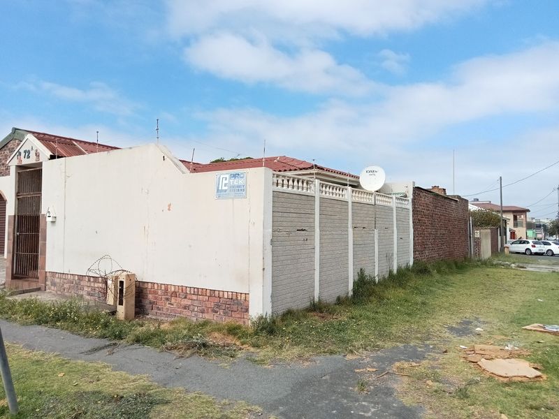 Front exterior view of the property featuring a perimeter wall, security gate, and tiled roof, showing signs of weathering and maintenance requirements.