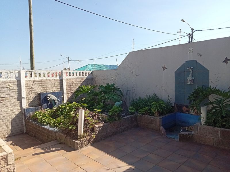 Outdoor patio area featuring tiled flooring, raised garden beds, and integrated water features against a boundary wall.