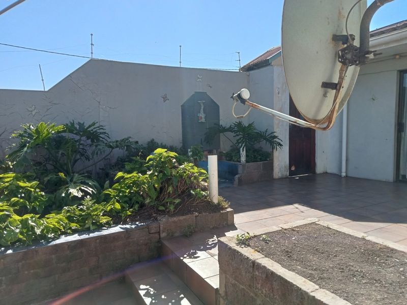Rear patio area featuring tiled flooring, brick planter boxes, and a wall-mounted water tank, requiring some maintenance and cosmetic updates.