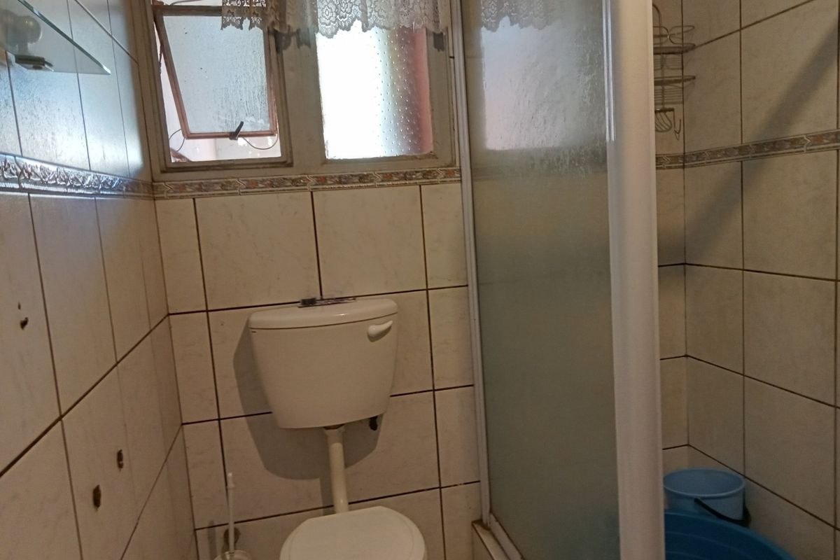 A compact bathroom featuring a toilet, shower enclosure, and tiled walls with a small window for ventilation.