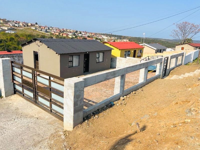 Front exterior view of a detached house featuring a corrugated metal roof, paved driveway, and a secure metal gate with a concrete perimeter wall.