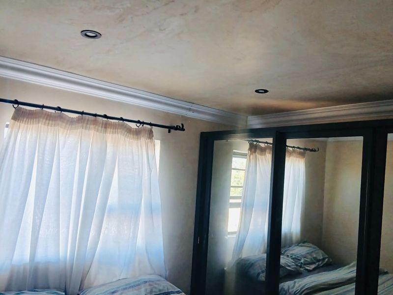 A bedroom featuring built-in cupboards with mirrored doors, recessed ceiling lighting, and decorative cornice detailing.