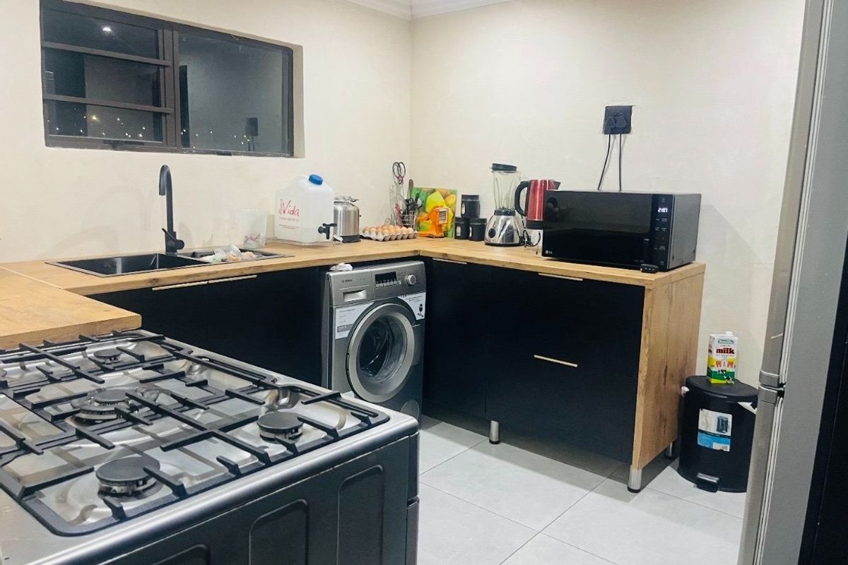 Modern kitchen featuring black cabinetry, wooden countertops, a gas hob, and an integrated washing machine with tiled flooring.