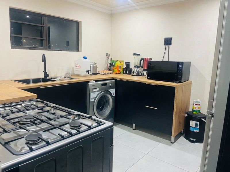 Modern kitchen featuring black cabinetry, wooden countertops, a gas hob, and an integrated washing machine with tiled flooring.