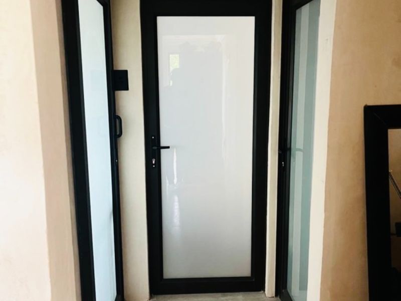 A clean, modern hallway featuring tiled flooring and multiple black aluminium framed glass doors with frosted panels.