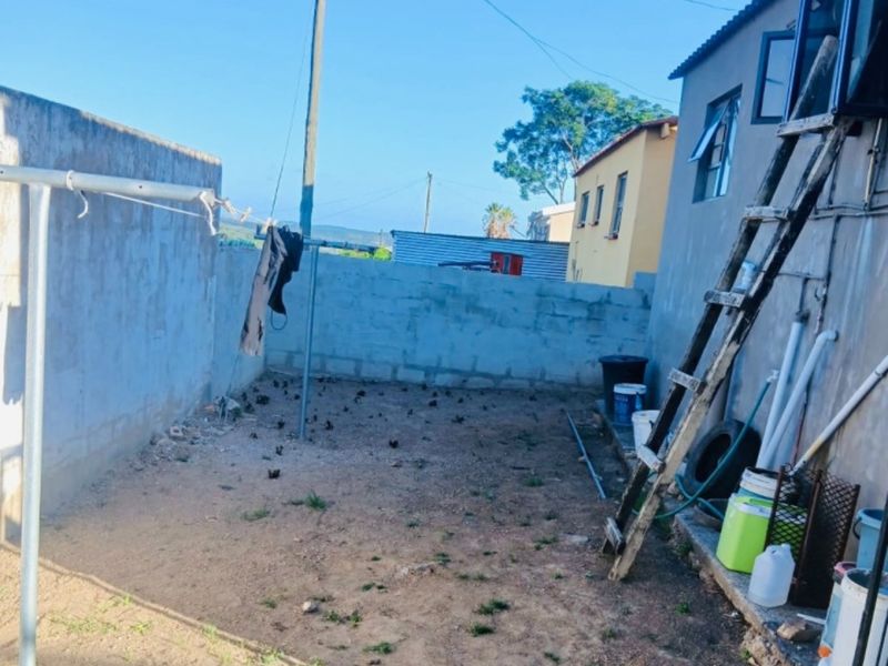 A rear exterior yard area featuring a concrete boundary wall, utility pole, and basic ground surface, offering potential for landscaping or outdoor improvement.