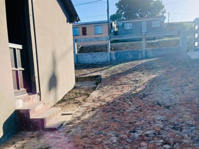 Rear exterior view showing a cobblestone paved area, concrete boundary wall, and access steps leading to the house entrance.