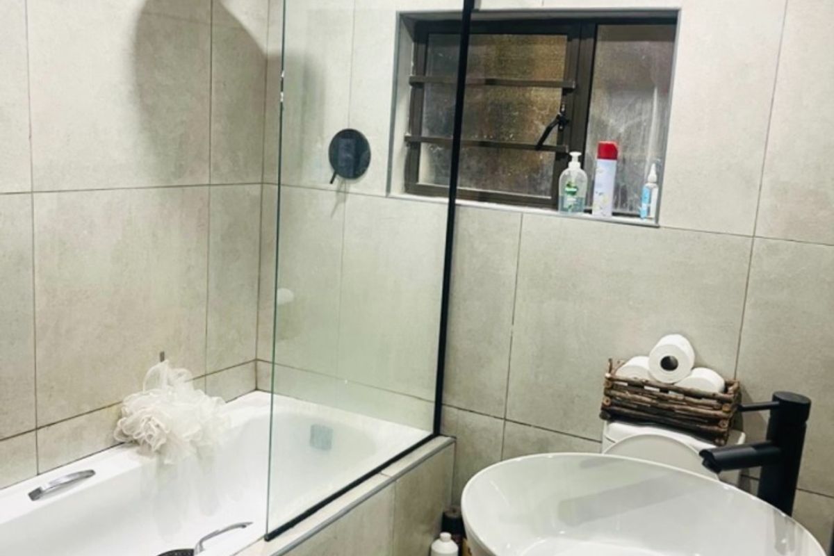 Modern bathroom featuring a vessel sink with black fixtures, a bathtub with a glass shower screen, and neutral wall tiling.