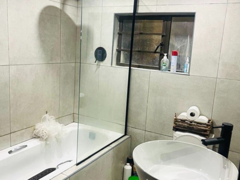 Modern bathroom featuring a vessel sink with black fixtures, a bathtub with a glass shower screen, and neutral wall tiling.