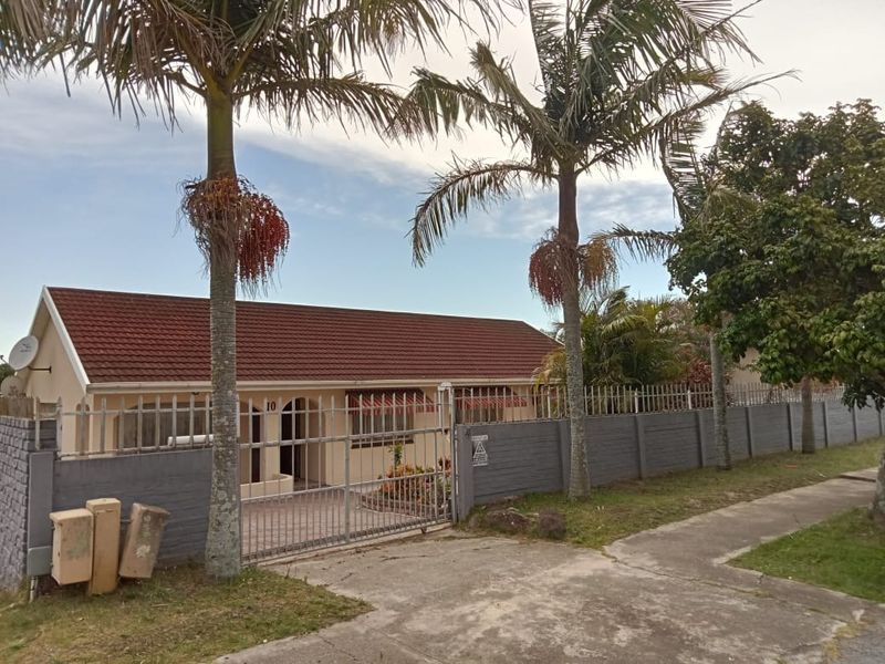 Front elevation of a single-story house featuring a tiled roof, perimeter wall with security gate, and established palm trees.