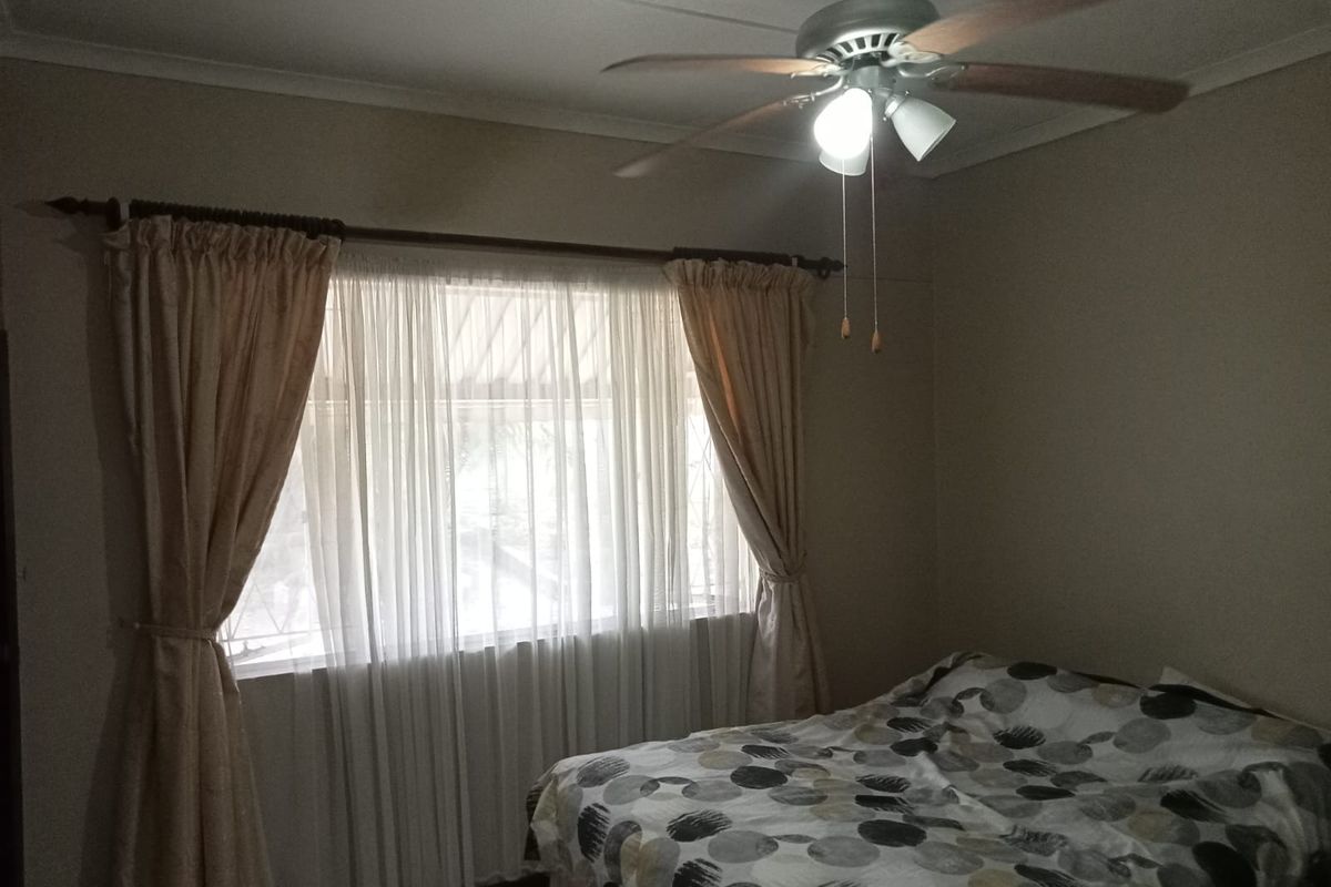 A bedroom featuring a ceiling fan and window with curtain rod, providing a functional space with neutral wall tones.