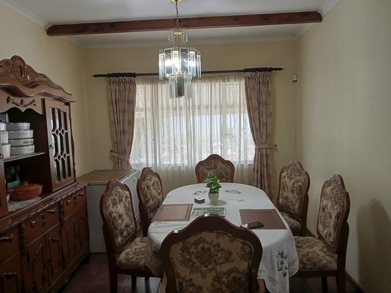 A traditional dining room featuring an exposed timber ceiling beam, a crystal chandelier, and tiled flooring.