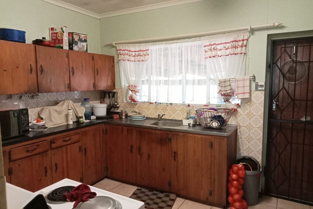 A dated kitchen featuring wooden cabinetry, laminate countertops, and a stainless steel sink, with visible ceiling water staining and traditional patterned wall tiles.