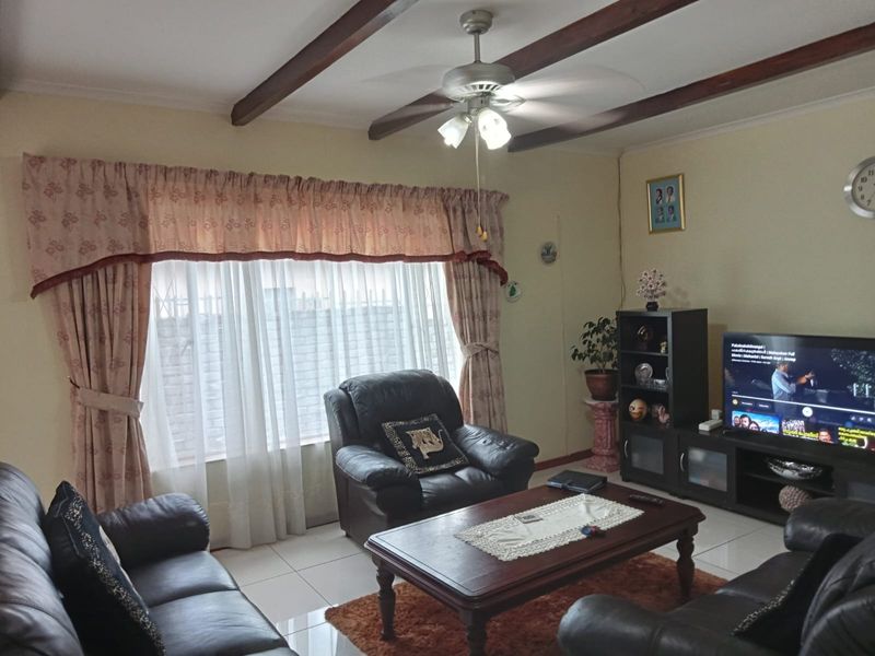 A comfortable living room featuring tiled flooring, exposed ceiling beams, and a central ceiling fan, providing a functional and well-lit space.