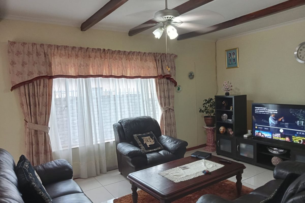 A comfortable living room featuring tiled flooring, exposed ceiling beams, and a central ceiling fan, providing a functional and well-lit space.