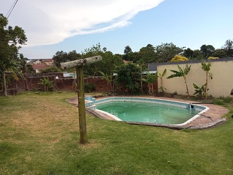 Outdoor pool area featuring a swimming pool with stone coping, set within a garden space enclosed by brick boundary walls.
