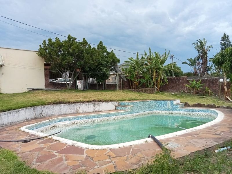 Outdoor pool area featuring a swimming pool with stone paving, a brick boundary wall, and a retaining wall in need of maintenance.