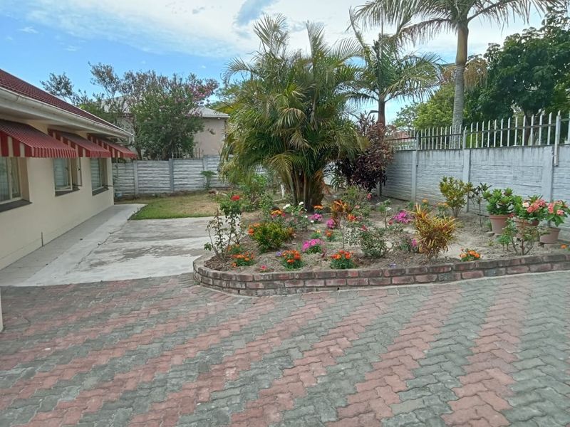 Rear exterior view featuring a brick paved driveway, concrete patio area, raised brick garden bed, and secure perimeter walling with metal spikes.