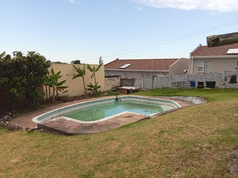 Outdoor backyard area featuring a swimming pool with stone paving, surrounded by a lawn and boundary walling.
