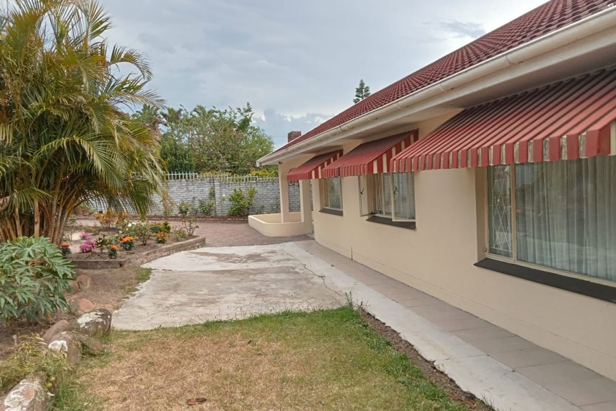 Rear exterior view of the house featuring a paved patio area, striped window awnings, and a garden with a brick boundary wall.