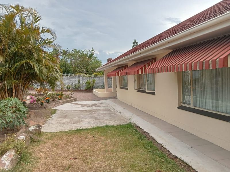 Rear exterior view of the house featuring a paved patio area, striped window awnings, and a garden with a brick boundary wall.