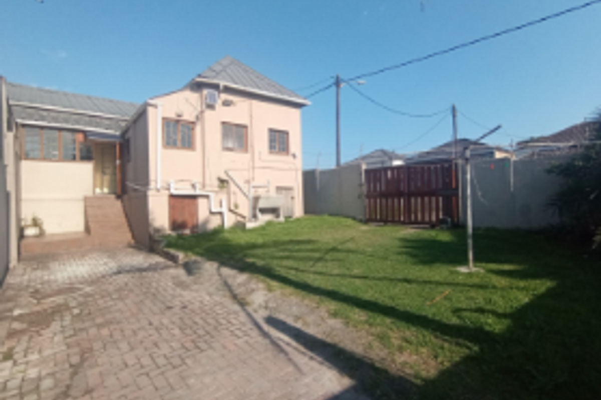 Rear view of the property featuring a paved driveway, a private lawn area, boundary walls, and an external staircase leading to the entrance.
