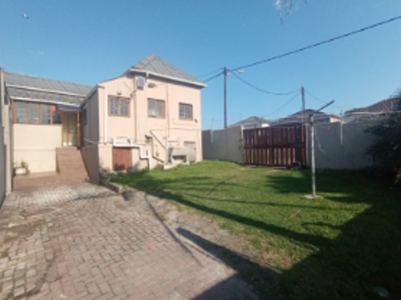 Rear view of the property featuring a paved driveway, a private lawn area, boundary walls, and an external staircase leading to the entrance.