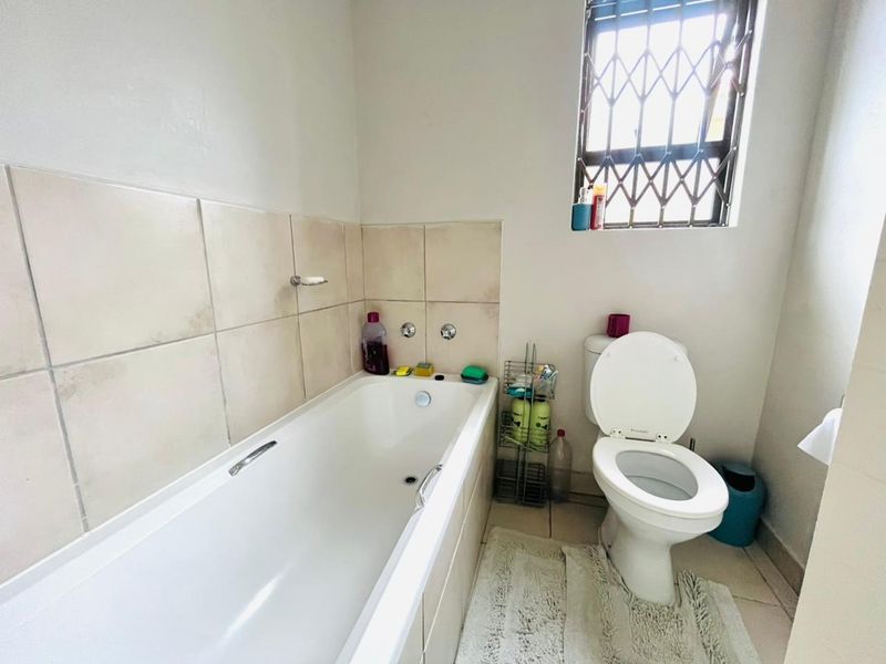 A functional bathroom featuring a standard bathtub, toilet, and tiled wall finishes with a window providing natural light.
